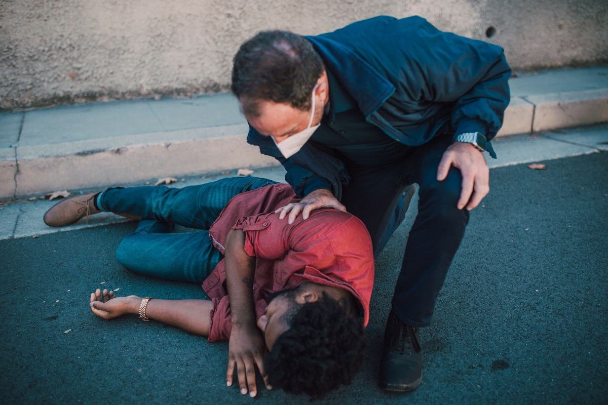 A responder kneeling beside a man lying on his side, checking on his welfare
