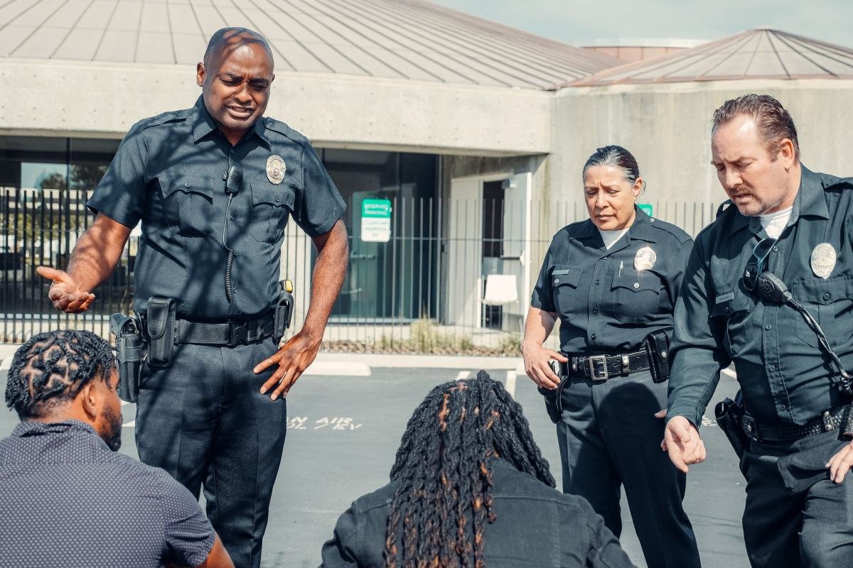 An officer speaking with people seated on the ground while colleagues stand by